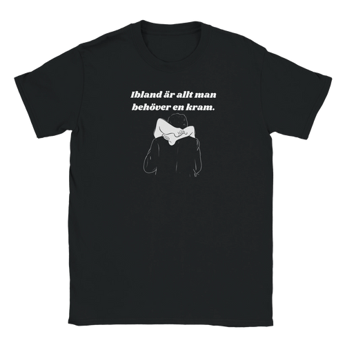 Svart t-shirt med texten "Ibland är allt man behöver en kram" ovanför ett minimalistiskt humoristiskt motiv med en dubbeltydig illustration av två personer.